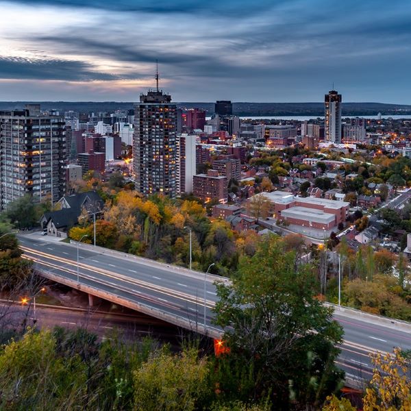View of a cityscape at dusk with high-rise buildings, a river in the background, and a highway in the foreground.