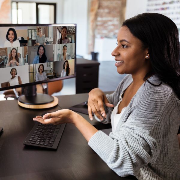 A woman participates in a video conference on her computer, with multiple participants visible on the screen.